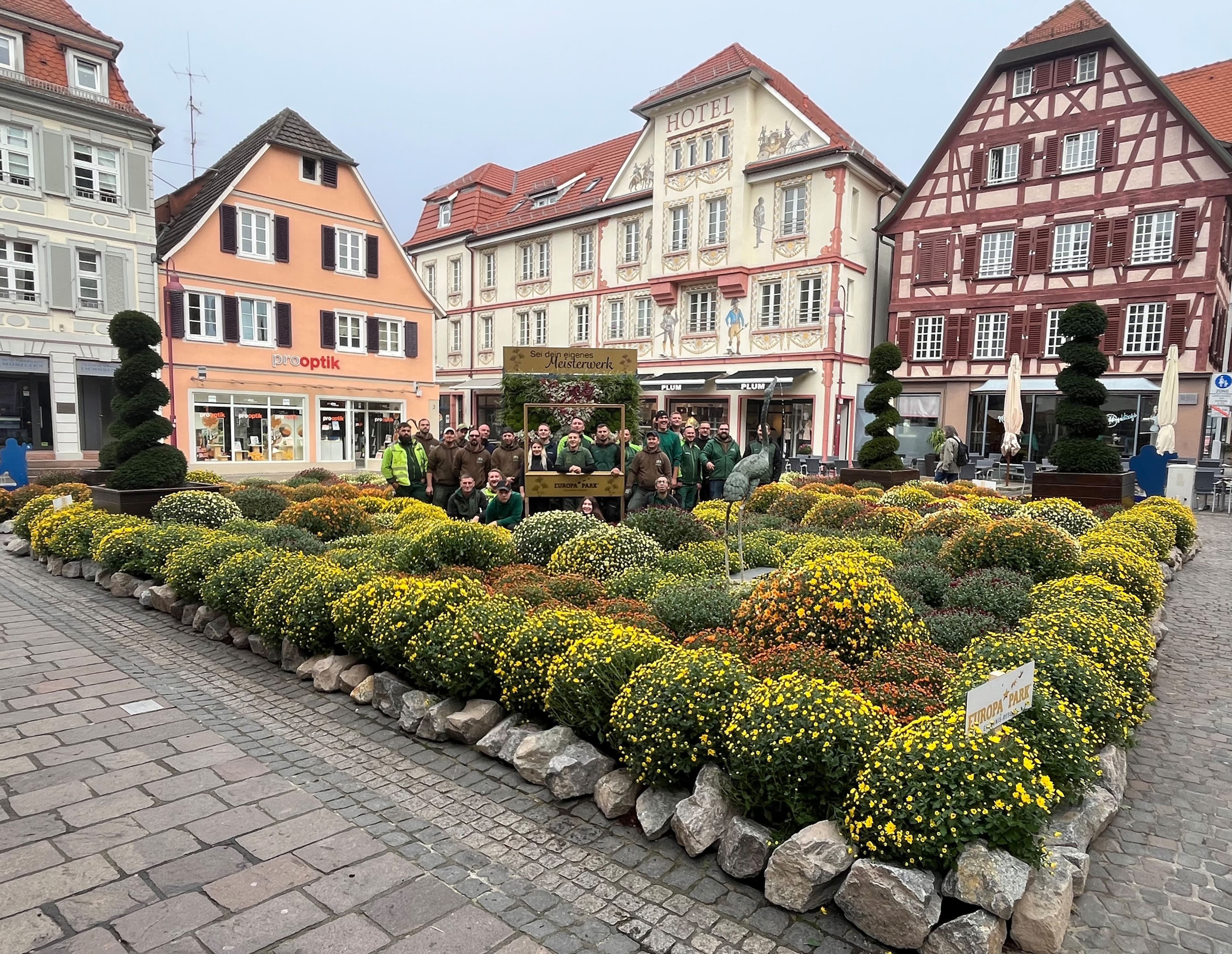 Das Europa-Park-Team gestaltet ein beeindruckendes Themenbeet auf dem Sonnenplatz in Lahr anlässlich der 25. Chrysanthema, das mit bunten Chrysanthemen und goldfarbenen Bilderrahmen kreative Fotomöglichkeiten bietet.
