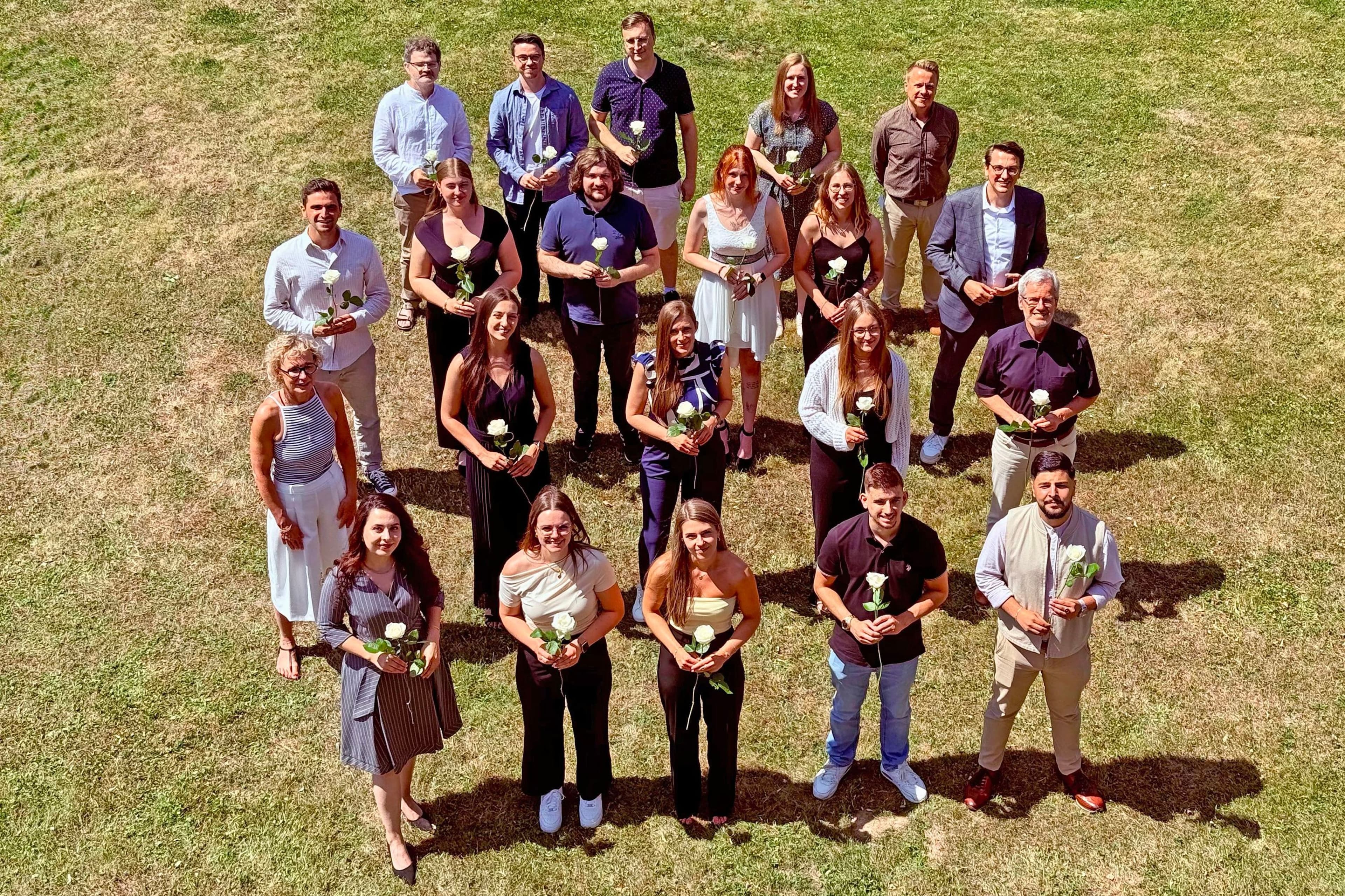 Leitungspersonen der Kreisverwaltung gratulieren Absolventinnen und Absolventen mit weißen Rosen und Geschenken.