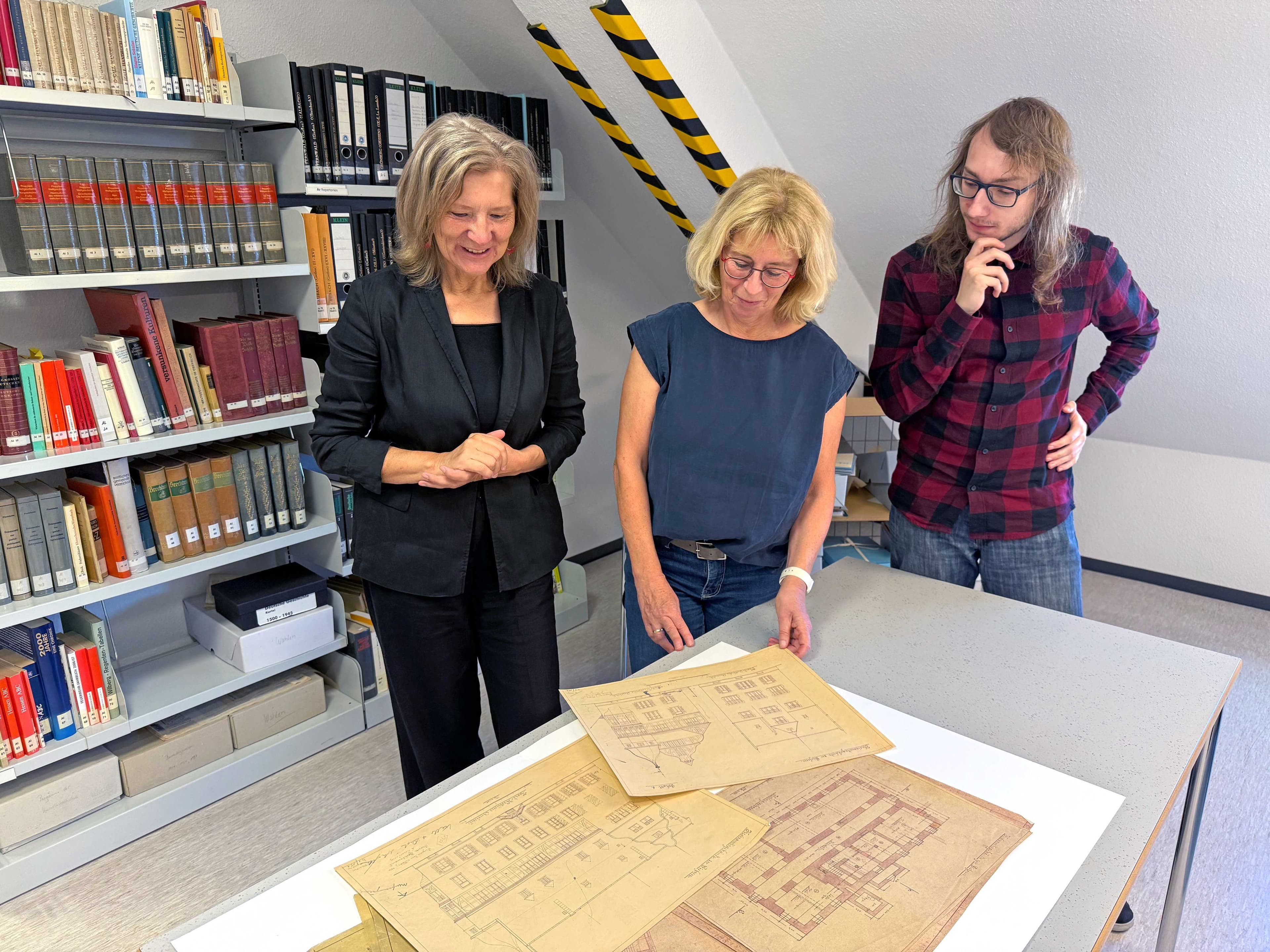 Landrätin Anita Schneider, Sabine Raßner und Alessio Garotti betrachten Baupläne im Kreisarchiv.