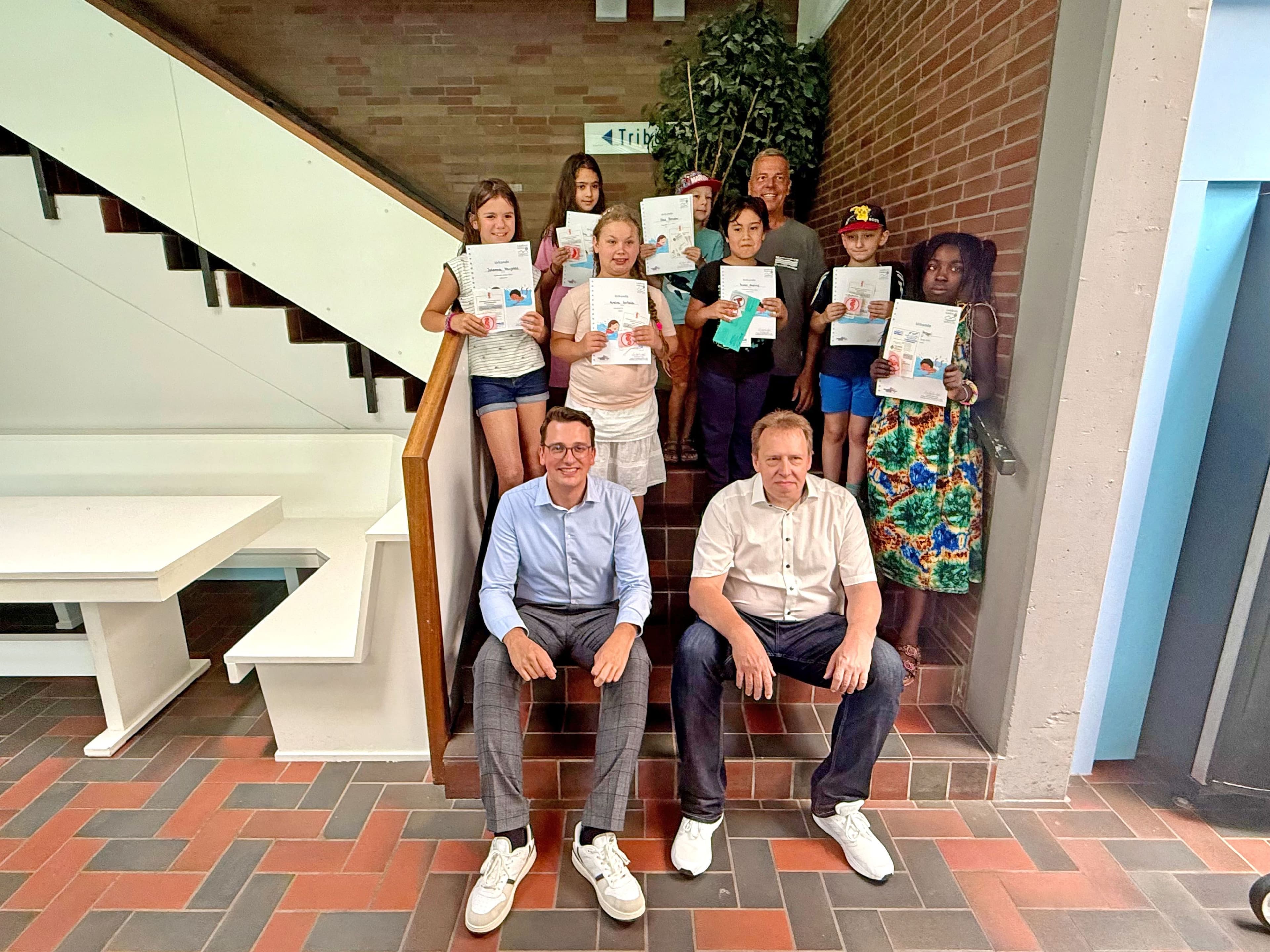 Christopher Lipp und Andreas Jung übergeben Teilnahme-Urkunden und Schwimmabzeichen an Kinder beim Schwimm-Camp.