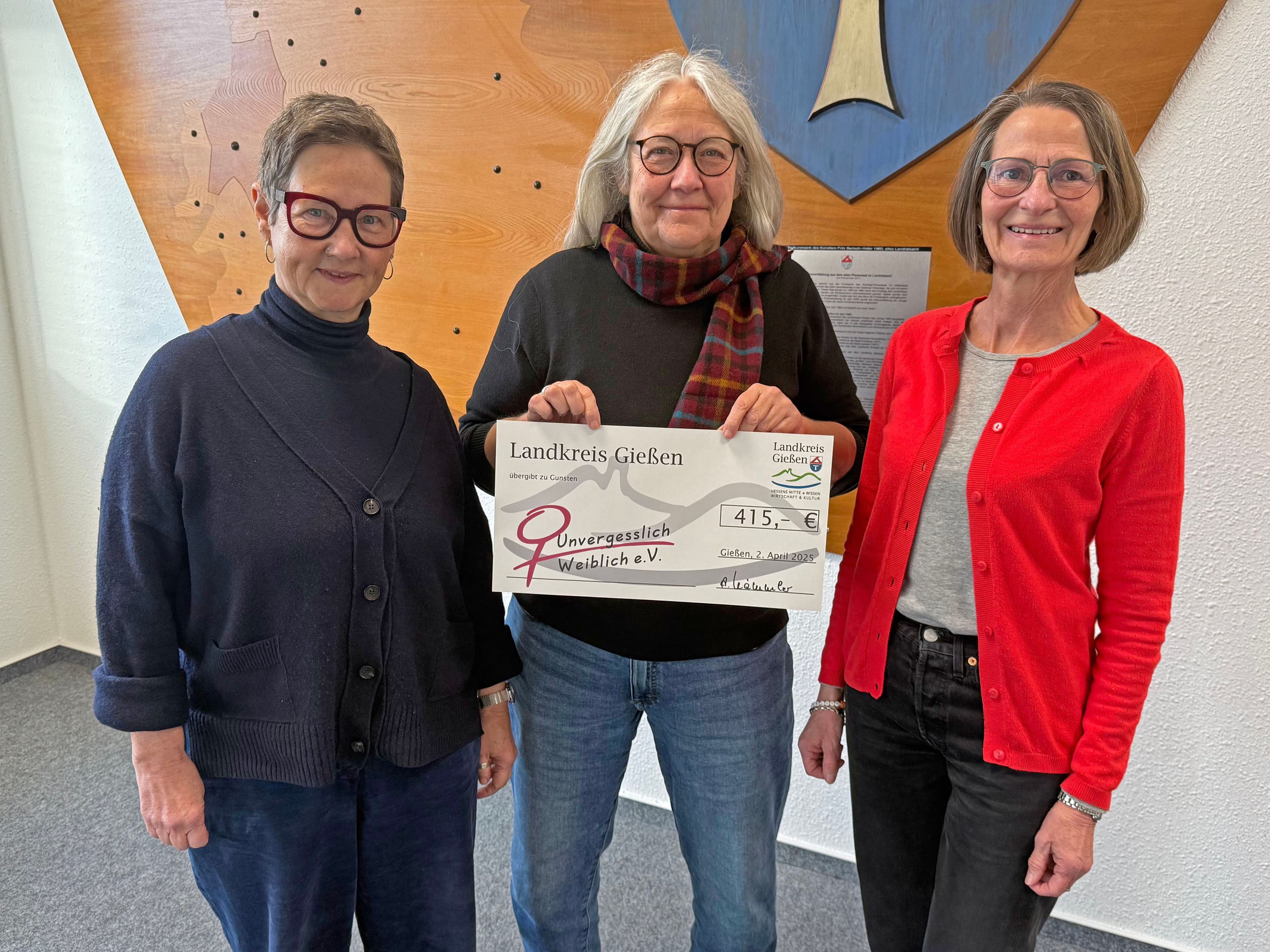 Doris Kroll und Nadine Seyler von 'unvergesslich weiblich' e.V. halten einen symbolischen Scheck über 415 Euro, der von Angelika Kämmler für den Verein bei einer Spendenveranstaltung übergeben wurde.