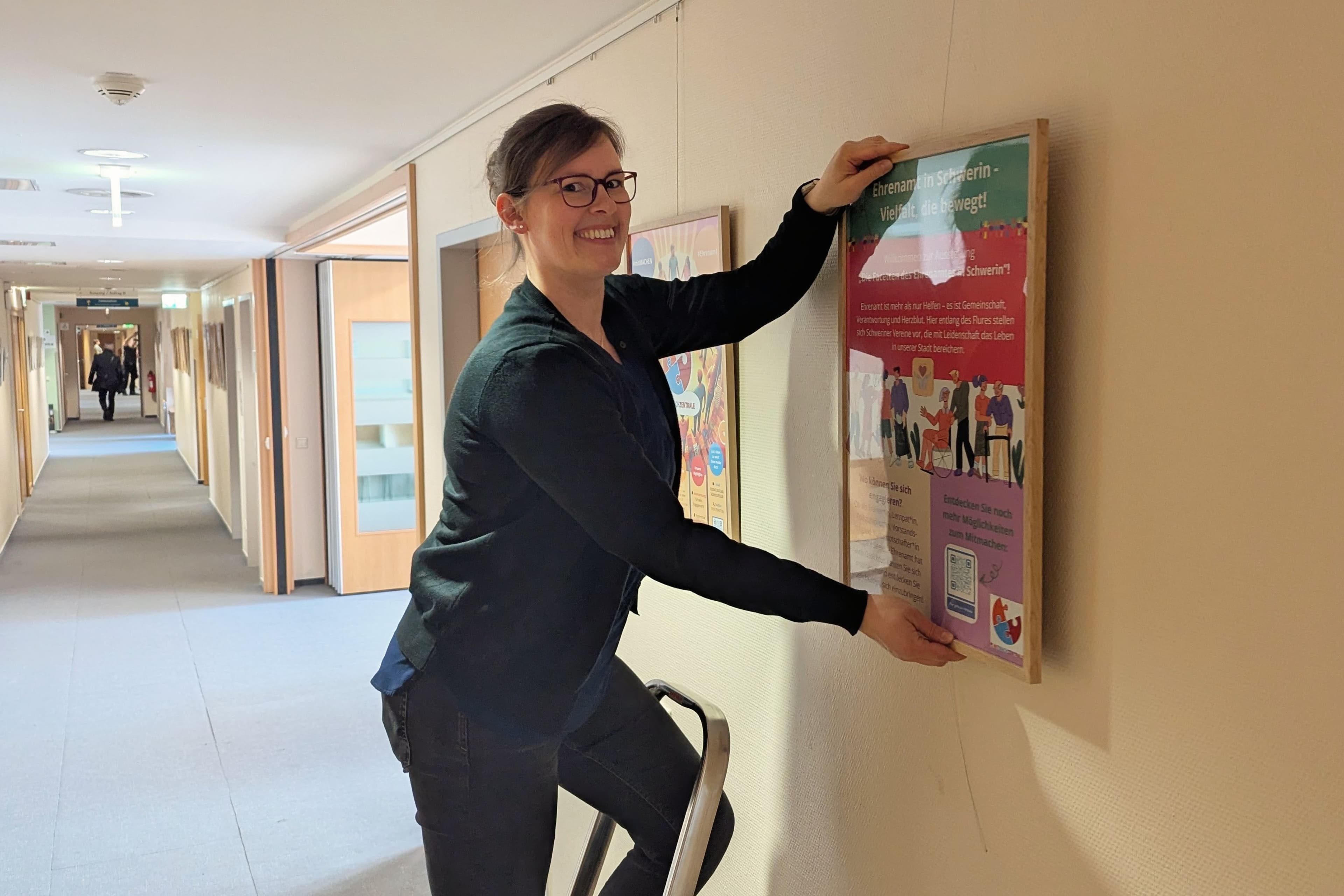 Romy Sadewasser von MitMachZentrale Schwerin hängt Plakate zur Ehrenamtsausstellung im Stadthaus auf.