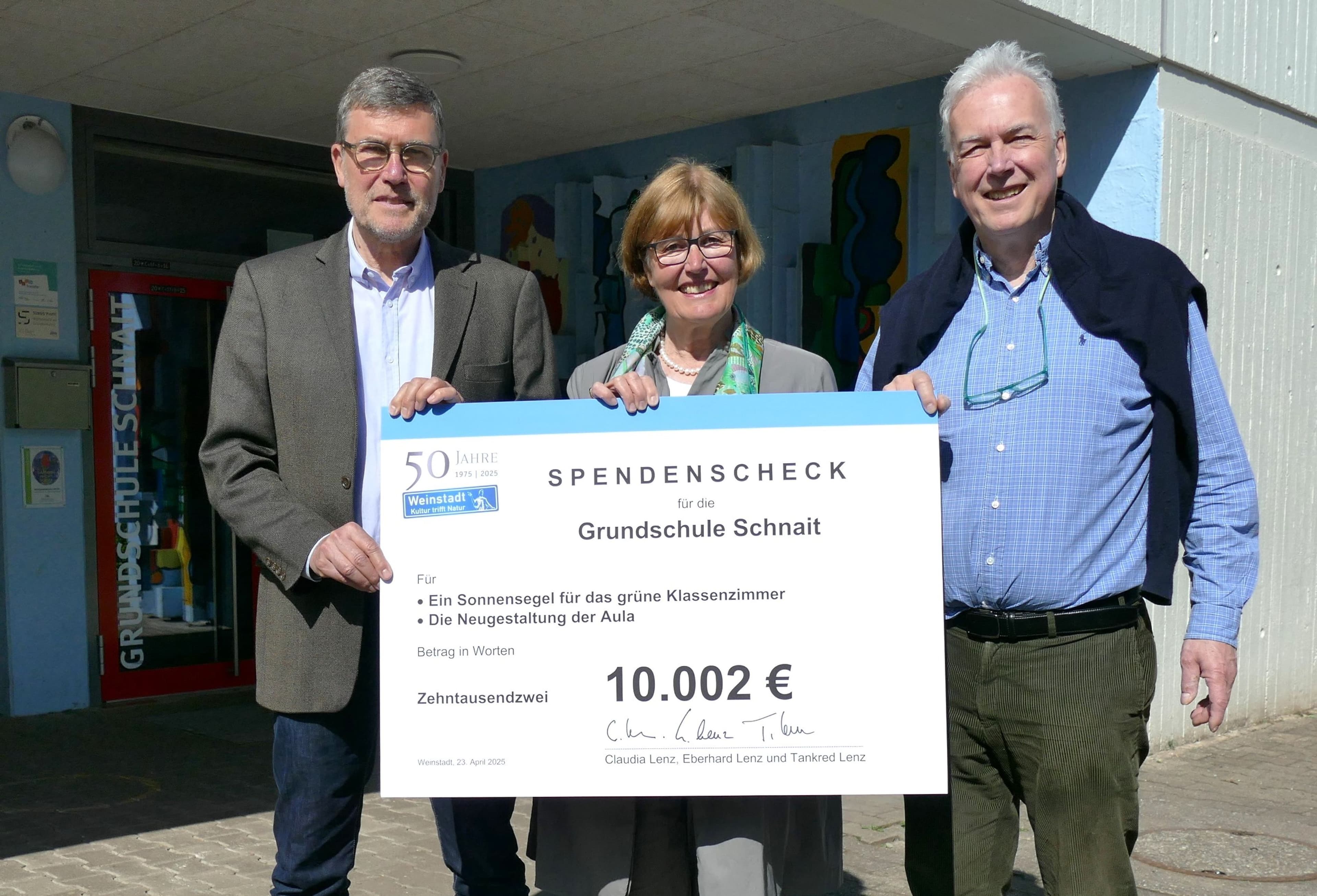 Geschwister Lenz übergeben einen Spendenscheck vor dem Eingang der Grundschule Schnait.