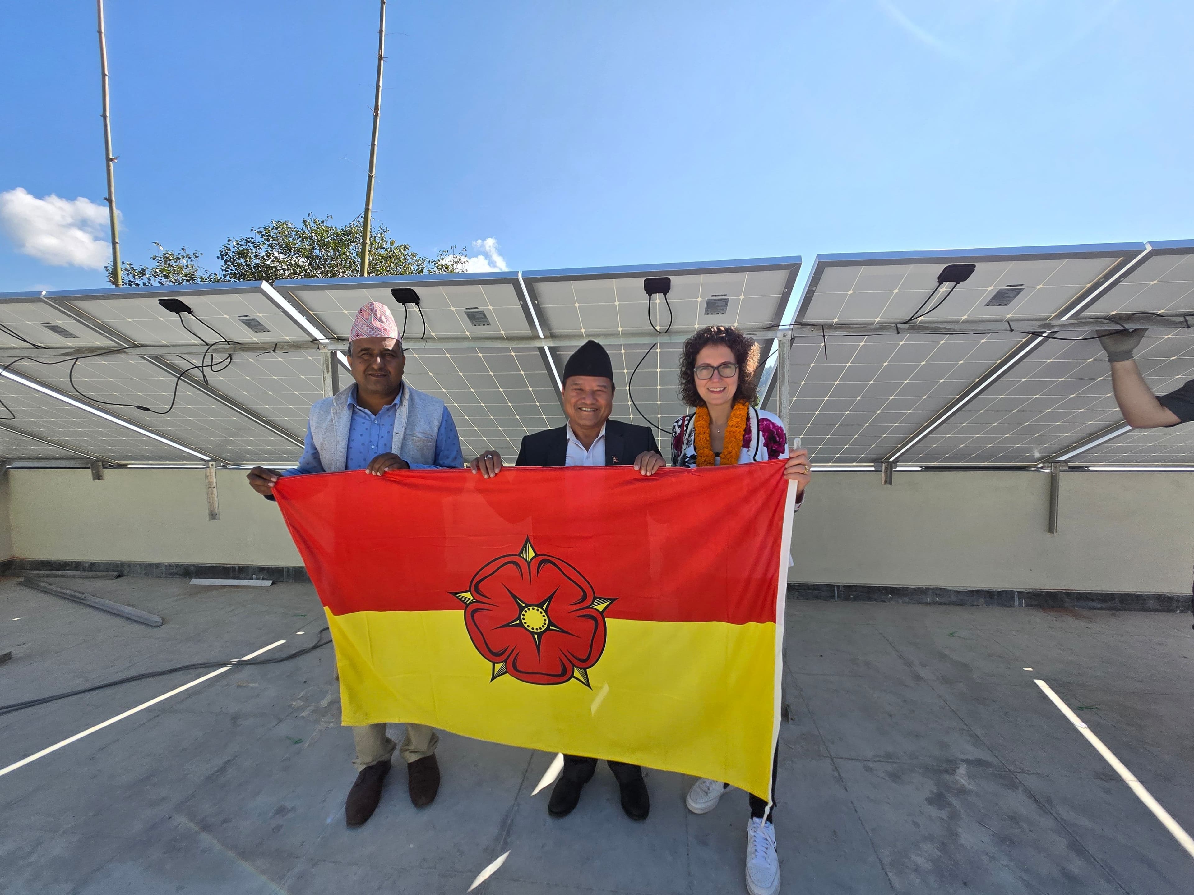 Nepalesische Gastgeber und die Detmolder Delegation präsentieren vor der Photovoltaikanlage die lippische Fahne.