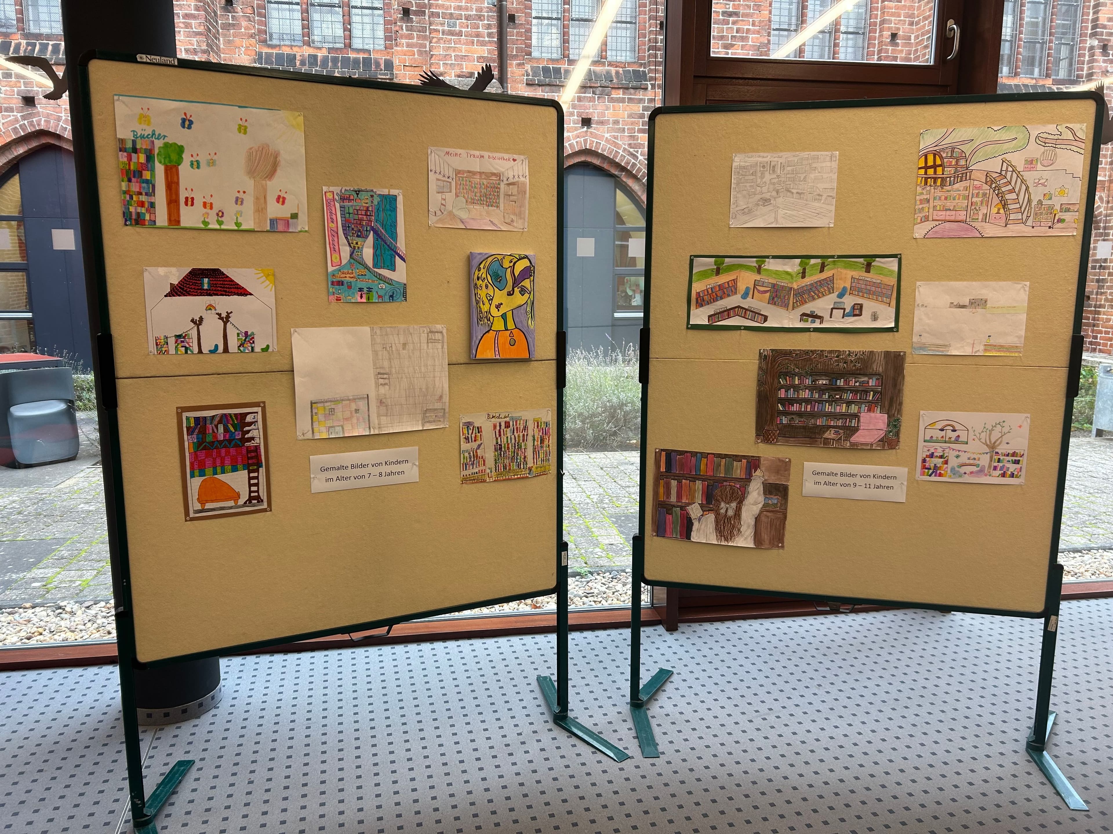 Jury und Bibliotheksleitung präsentieren die sechs Gewinnerbilder des Malwettbewerbs zum Bibliotheksjubiläum.