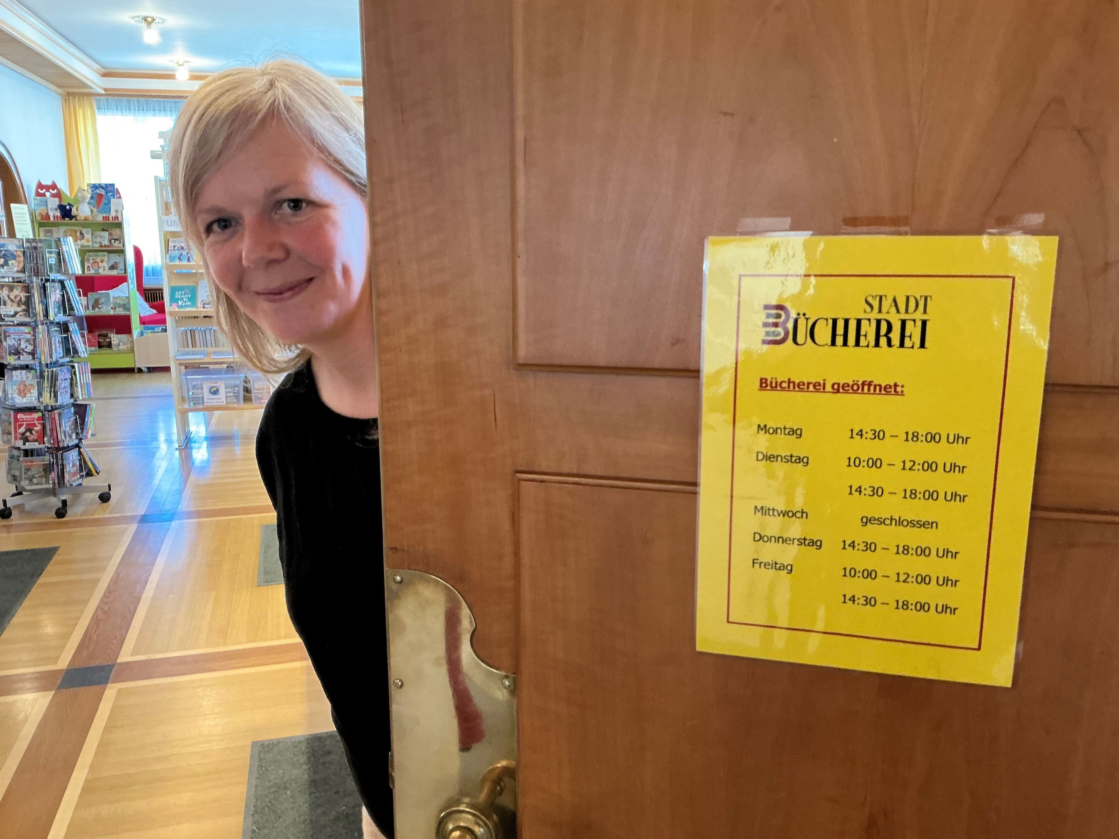 Stadtbücherei-Mitarbeiterin Sarah Roller steht am Eingang der Bibliothek vor ausgehängten Öffnungszeiten.