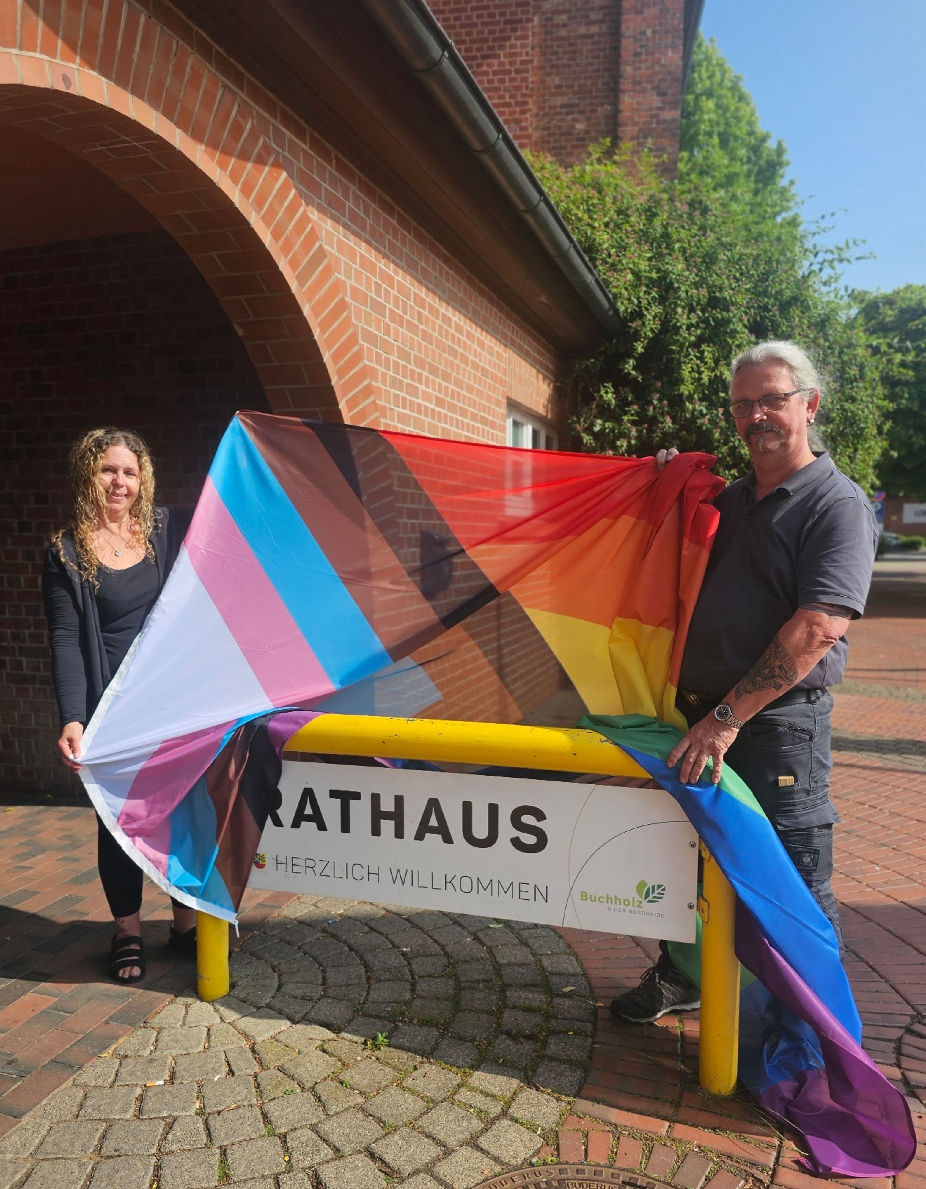 Gleichstellungsbeauftragte und Hausmeister hissen die Regenbogenflagge vor dem Rathaus Buchholz.